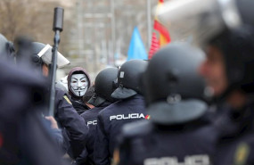 ep agentes de la policia nacional frente a los manifestantes con mascaras de anonymous y banderas de