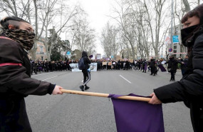 ep dos mujeres con la cara tapada que sujetan un palo con una bandera morada ante la manifestacion