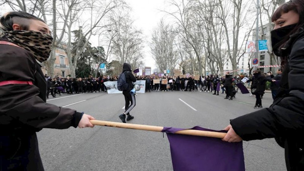 ep dos mujeres con la cara tapada que sujetan un palo con una bandera morada ante la manifestacion