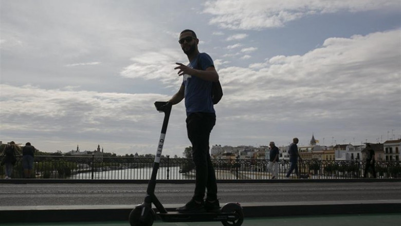 Imágenes de recursos de patinetes eléctricos. Joven paseando por el Puente de Triana en patinete eléctrico. | María José López - Europa Press ep imagenes de recursos de patinetes electricos joven paseando por el puente de triana en patinete
