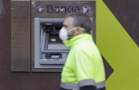 ep un trabajador con chaleco y mascarila pasa delante de un cajero de bankia