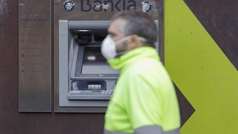 ep un trabajador con chaleco y mascarila pasa delante de un cajero de bankia